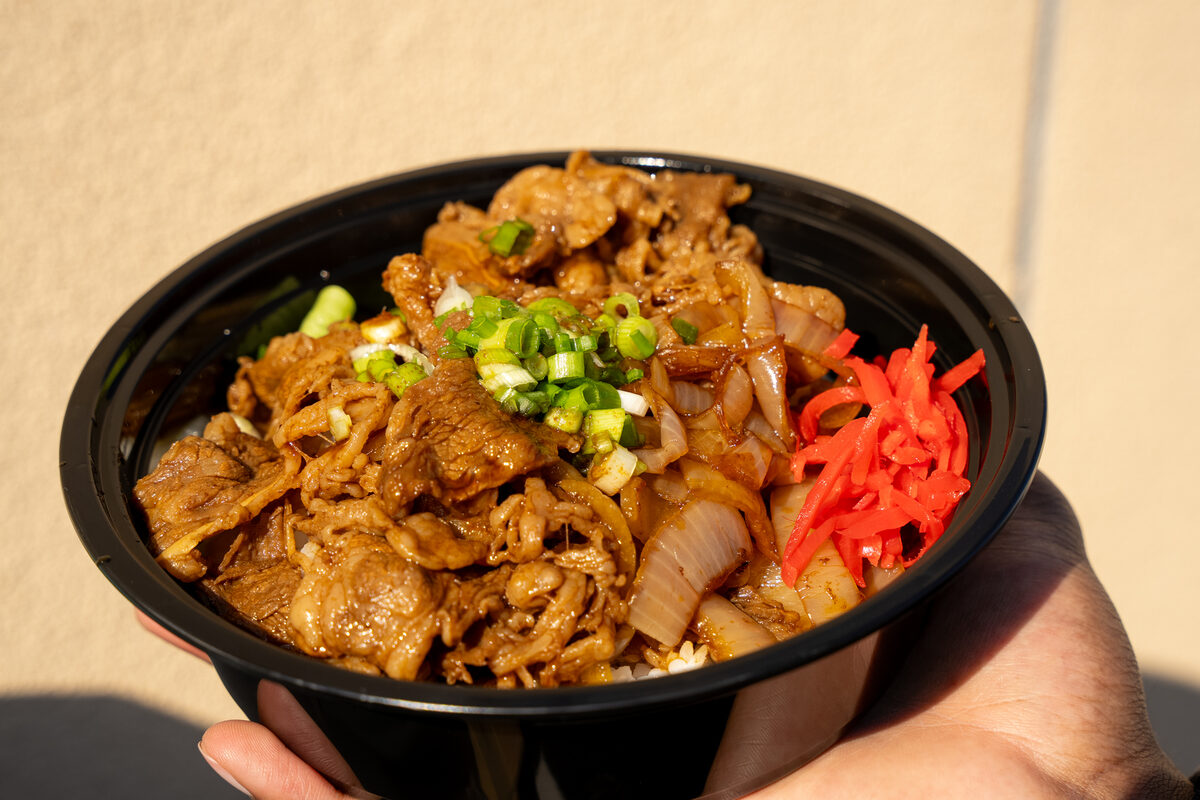 A rice bowl topped with sliced beef, scallions, and pickled ginger